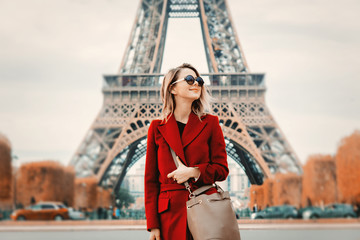 Style redhead girl in red coat and bag at parisian street in autumn season time. Eiffel tower on background - obrazy, fototapety, plakaty