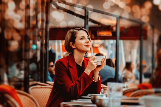 Style redhead girl in red coat with cup of coffee in parisian cafe. Autumn season time
