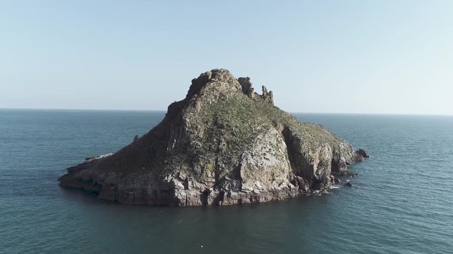 Aerial drone shot rotating around thatcher rock off the coast of England on the ocean during a bright and sunny day