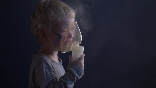 Caucasian blond child is crying from spasm of bronchitis and inhales vapors containing medications from inhaler to stop choking. Medical procedures. Respiratory medicine. Bronchitis, asthmatic problem