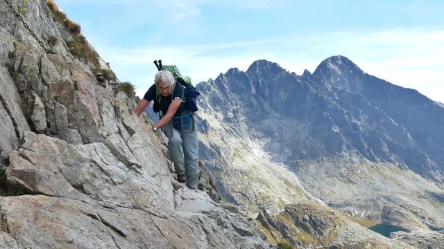 Active senior hiker climbing on a tricky trail in the mountains, mountains in the background (high tatras, slovakia)