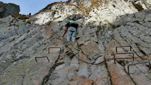 View from below: A person climbing up to the pass using steps and chains to climb. (high tatras, slovakia)