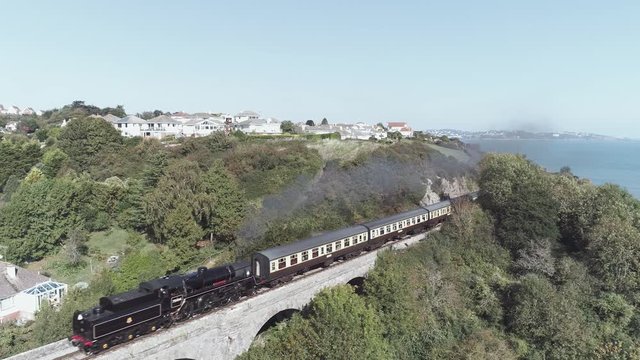 Aerial drone view of a passenger steam train passing on a stone bridge in the rural countryside of England, Devon, United Kingdom