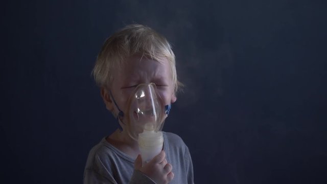 Caucasian blond child is crying from spasm of bronchitis and inhales vapors containing medications from inhaler to stop choking. Medical procedures. Respiratory medicine. Bronchitis, asthmatic problem