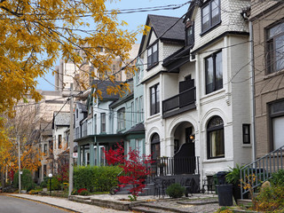 street of historically designated old Victorian houses with gables and painted brick, downtown Toronto, with large office building in background