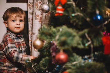 Baby boy standing beside Christmas tree at home