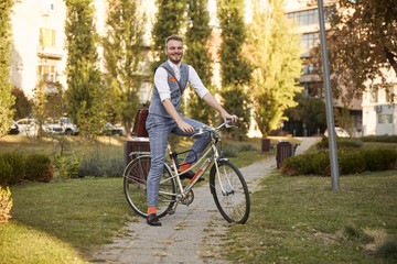 one young smiling man, 20-29 years old,  wearing hipster suit, smart casual, posing sitting on a old city bike in park road trail.