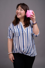 Mature beautiful Asian businesswoman holding piggy bank