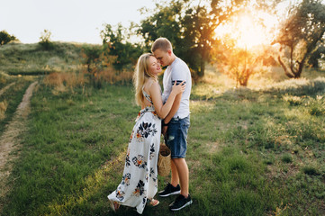 Stylish guy and a young girl hugging against the backdrop of nature and sunset with backlight. Portrait of beautiful newlyweds.