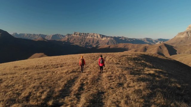 Aerial view of a two girls traveler with backpacks and cameras stroll through the hills between the epic rocks in the mountains. Girls photographers with their cameras at sunset