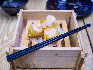 The​ shrimp chinese steamed dumpling​ in​ Dim Sum wooden steamer and​ black​ chopsticks on​ the​ table​ which​ it is in a Chinese restaurant.