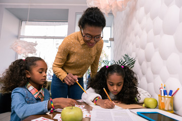 Nursery teacher. Beautiful nursery teacher wearing glasses and yellow blouse standing near cute preschoolers