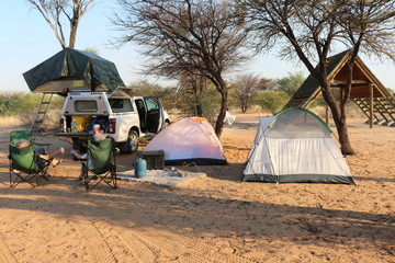 A campsite in Mabuasehube National Park in Botswana showing tents and people relaxing on camping chairs.