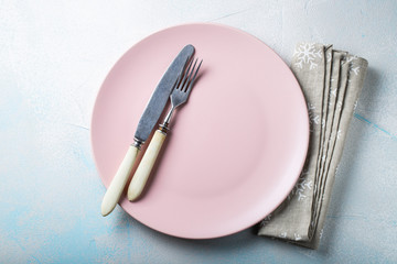 Pink empty plate with Cutlery and beige towel with snowflakes on blue stone background. Top view with copy space. Flat lay