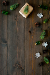 Background with New Year gift. Box wrapped in craft paper, decorated with pine sprig and cones on dark wooden background top view space for text