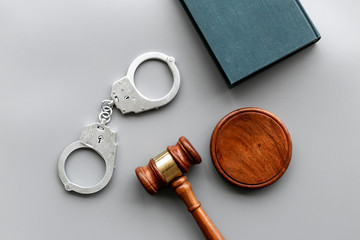 Arrest concept. Metal handcuffs near judge gavel and law book on grey background top view