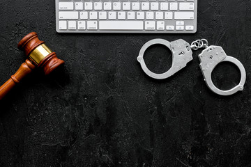 Arrest of a hacker for cyber fraud concept. Handcuff near keyboard and judge gavel on black...