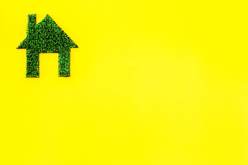 Eco friendly technologies for home concept. House silhouette made of green grass on yellow background top view copy space