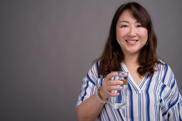 Mature beautiful Asian businesswoman holding glass of water