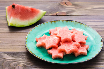 Pieces of watermelon in the form of stars on a ceramic plate and a large piece of watermelon on a wooden table