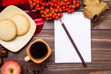 Autumn still life - coffee, cookies, a plaid, a notebook and a pencil on a wooden background. Top view