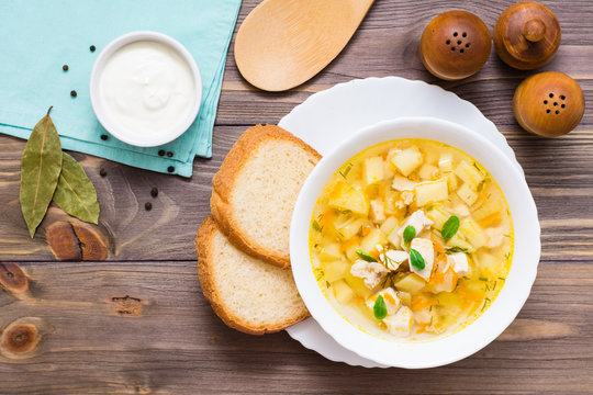 Fresh chicken broth soup with potatoes and herbs in a white bowl on a wooden table. Top view