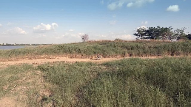 aerial panning drone shot of an old woman pushing up his bicycle on a  sandy dirty road 