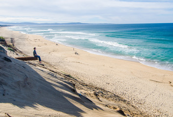 Man Sitting on Pipe looking at Sand Beach