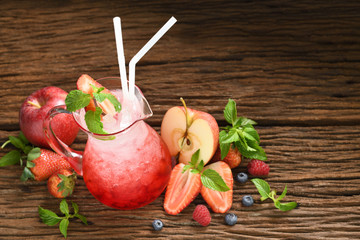 Mixed fruit juice with syrup and soda in glass pitcher surrounded by fruits on wooden background