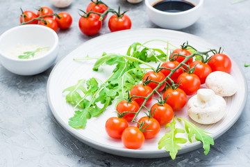 Сherry tomatoes, mushrooms, arugula on a plate, sesame and balsamic sauce in a bowls
