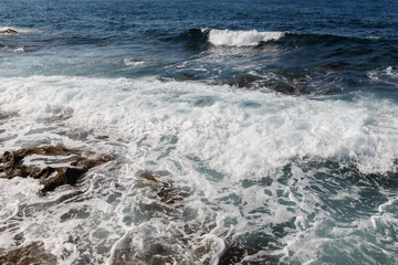 sea waves are broken by splashes and white foam on huge rocks in the warm Mediterranean sea in which boats and yachts