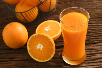 Fresh orange juice in tall glass with basket of oranges on wooden table