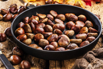 Roasted chestnuts served in chestnut pan on an old table