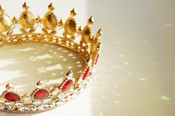 Golden crown with red and white diamonds magically lighted up with sun rays, decorative shadow and colorful flares on white table  © photokozyr