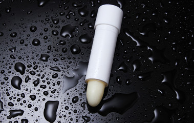 Hygienic lipstick on a black background with water drops.