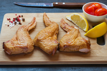 Smoked chicken wings on a wooden chopping Board with vegetables. Dark background
