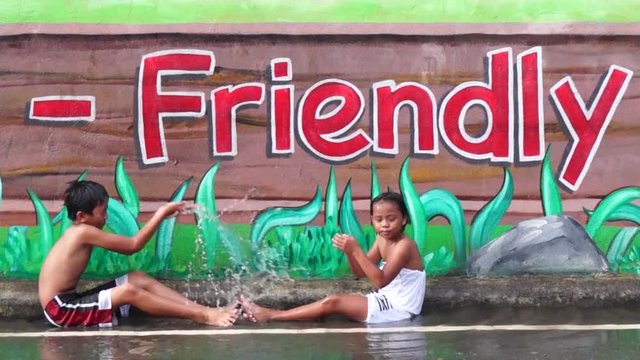 Children enjoy bathing in the rain in front of mural painted wall