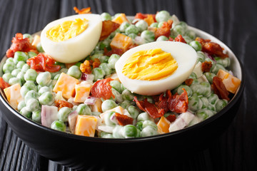 English cuisine pea salad with boiled eggs, onions, bacon and cheddar cheese with sauce close-up in...