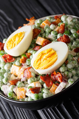 English salad of fresh green peas with eggs, bacon and cheese dressed with cream sauce close-up in a bowl. vertical