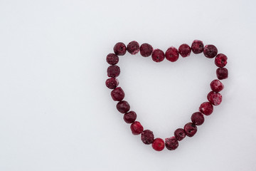 Frozen red cherries laid out in the shape of a heart on white snow background
