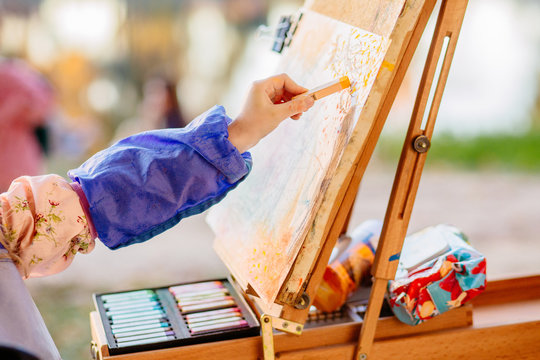 Close up of child's hand painying on easel with crayon outdoor in sunset autumn time.