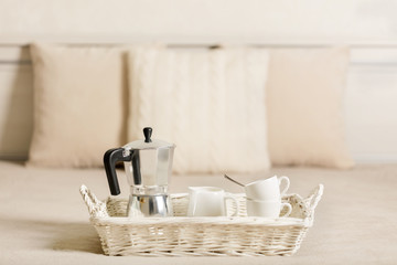 Breakfast in bed. On a white wicker tray there is a coffee maker, coffee white cups.