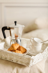 Fototapeta na wymiar Breakfast in bed. On a white wicker tray there is a coffee maker, coffee white cups and croissants.