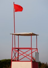 Fototapeta na wymiar Lifeguard sighting tower with red waving flag means danger