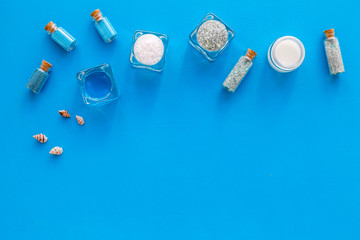 Dead sea cosmetics layout. Sea salt in bottles and bowls near small shells on blue background top view copy space
