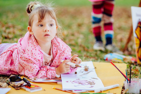 Cute dreamer little girl artist learn to drawing, children painting in autumn park. Open air activity for preschool age children kindergarten concept.