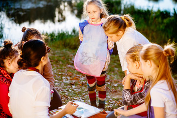 Female paitner artist teaching group of children outdoor on lake shore in autumn summer day. Open air activity for school age children concept.