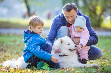Father with preschool son and baby daugther playing with samoyed dog in autumn park