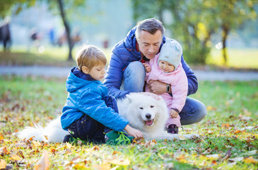 Father with preschool son and baby daugther playing with samoyed dog in autumn park