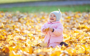 Cute baby girl playing with leaves and laughing in autumn park